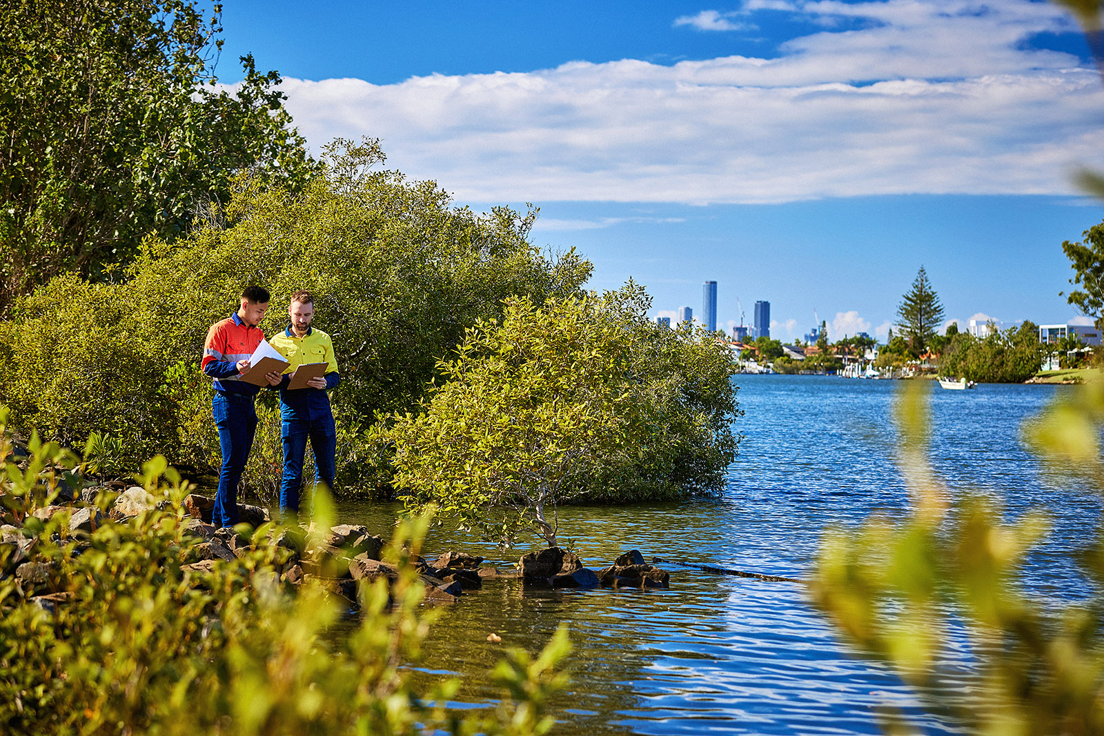 Two men compare notes while standing on rocks on a river bank