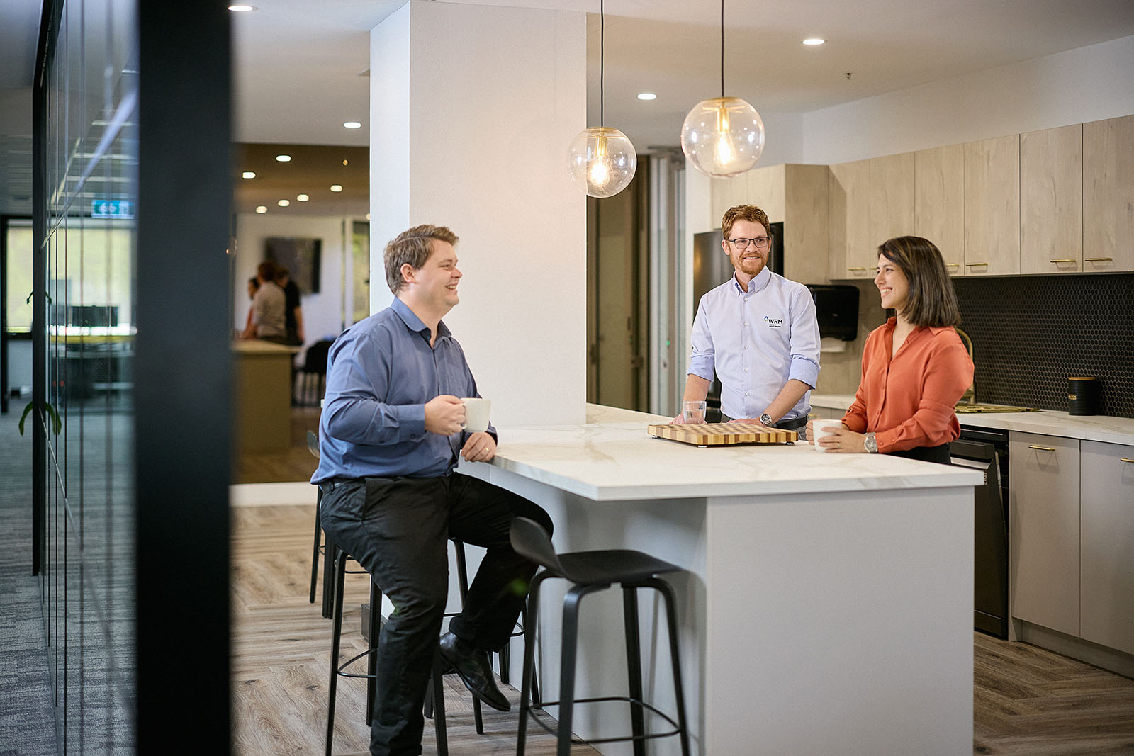 Three people talk amiably in an office kitchen